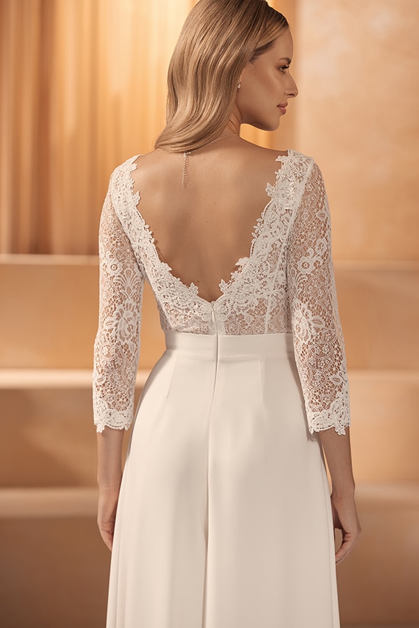 Eine blonde Frau im cremefarbenen Kleid mit Spitzenärmeln zeigt ihren Rücken