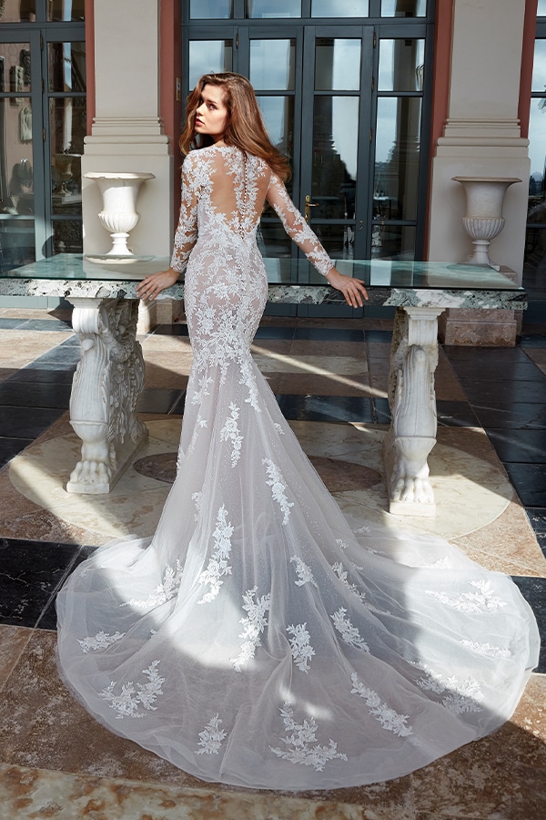 Eine braunhaarige Frau im eleganten weißen Spitzenkleid blickt ernst zurück