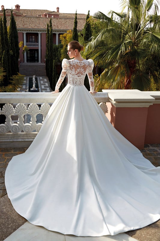 Eine elegant gekleidete Frau im weißen Brautkleid steht vor einer Villa und schaut entspannt in die Ferne
