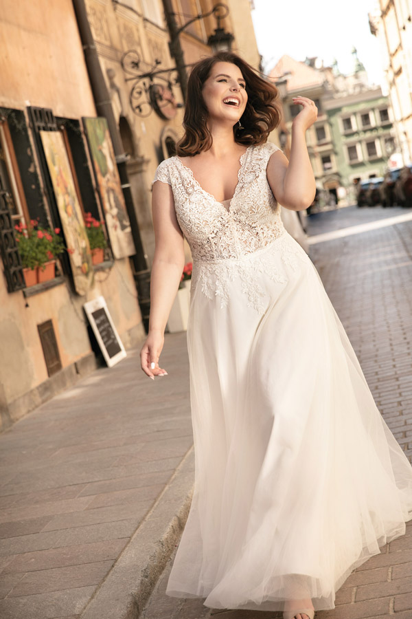 Eine lächelnde Frau im weißen Brautkleid geht selbstbewusst durch eine Altstadtstraße