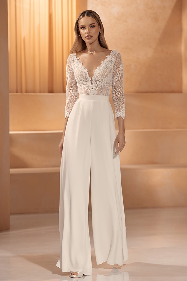 Eine lächelnde Frau mit langen blonden Haaren trägt einen eleganten weißen Spitzenoverall