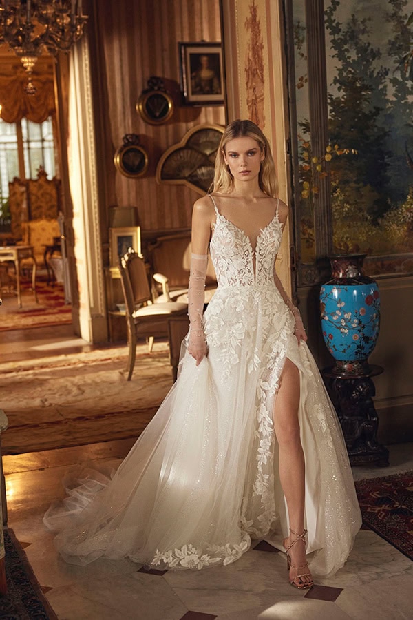 Eine junge Frau mit ernstem Blick trägt ein elegantes weißes Hochzeitskleid mit Blumenmuster