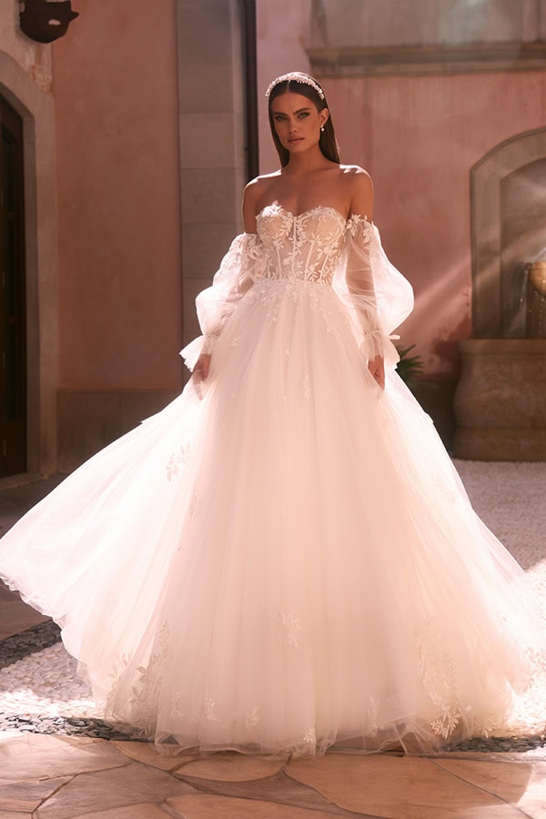 Eine Frau in einem eleganten, weißen Brautkleid mit Spitzen und Kopfschmuck lächelt sanft