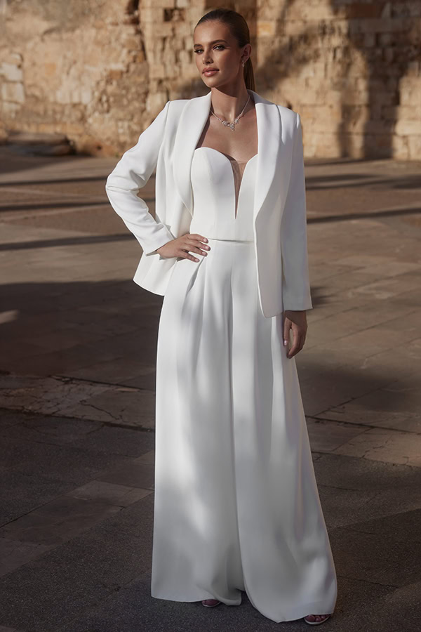 Eine elegant gekleidete Frau in einem weißen Hosenanzug mit entspanntem Blick