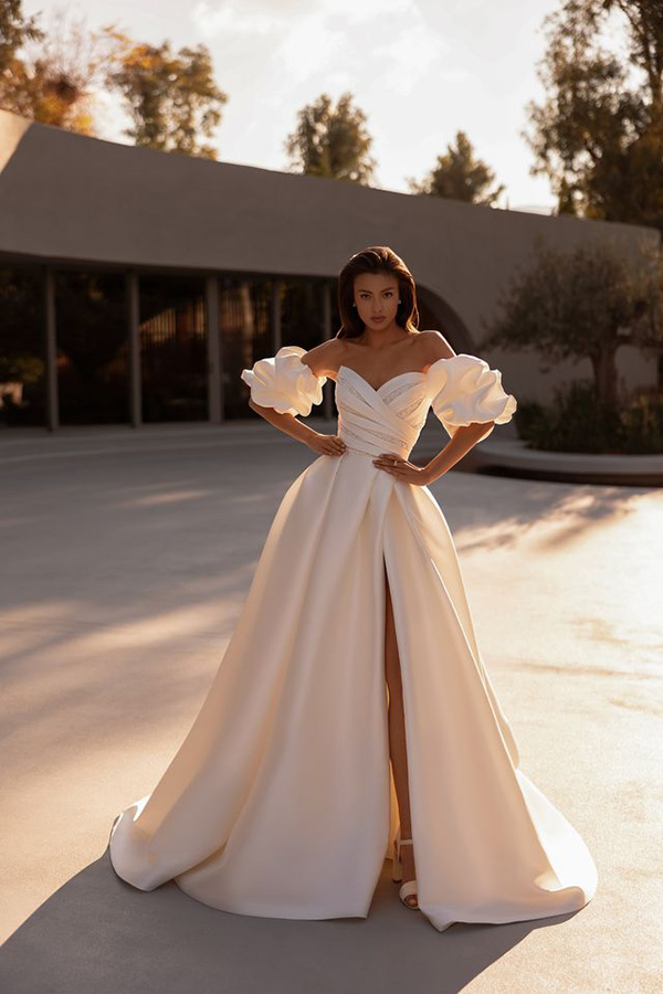 Frau mit ernstem Blick trägt ein elegantes weißes Kleid mit voluminösen Ärmeln