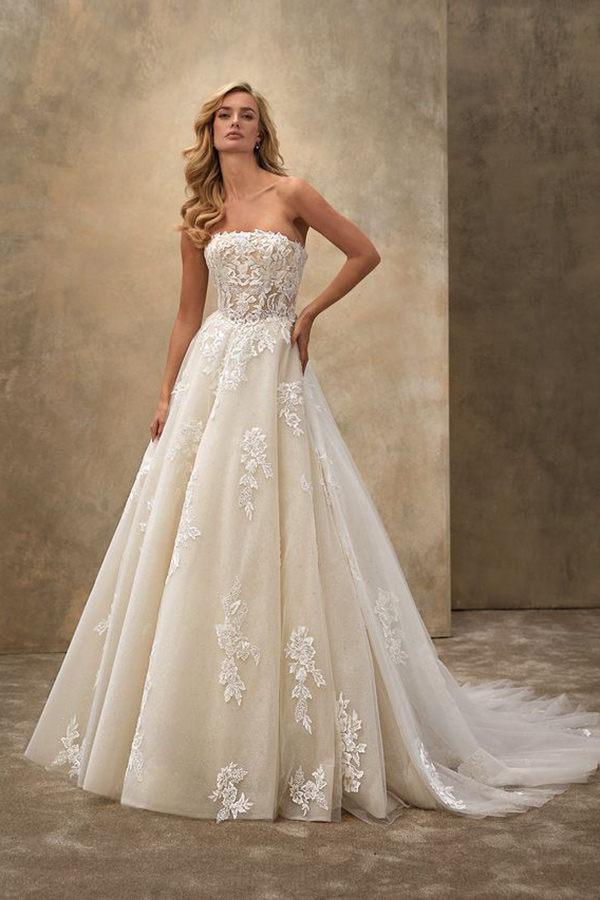 Eine blonde Frau mit ernstem Blick trägt ein cremefarbenes Spitzenhochzeitskleid