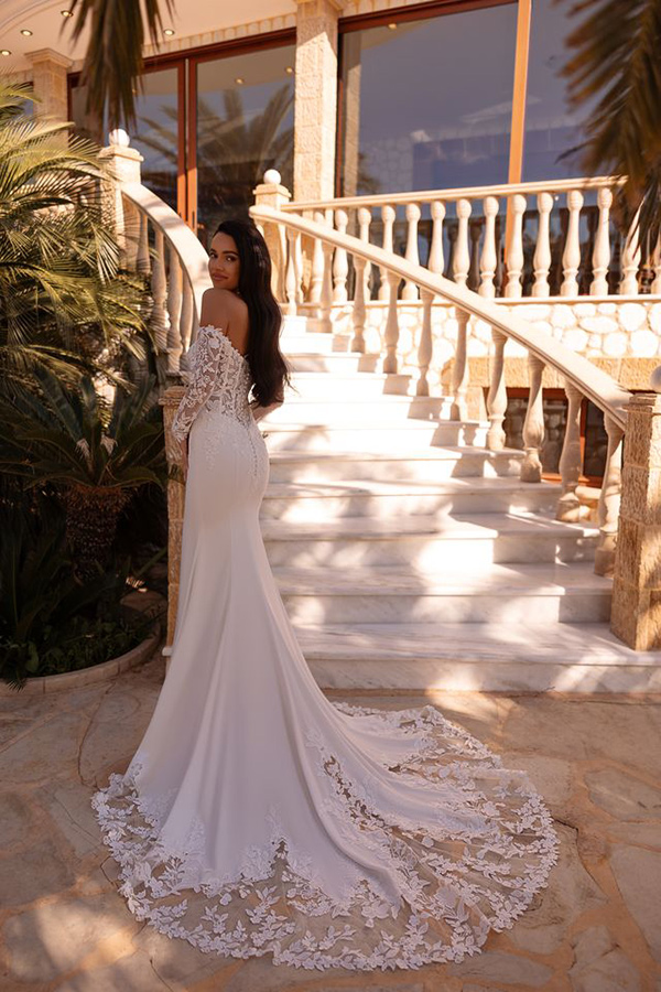 Eine Frau mit langen dunklen Haaren trägt ein elegantes weißes Brautkleid und blickt ruhig zurück