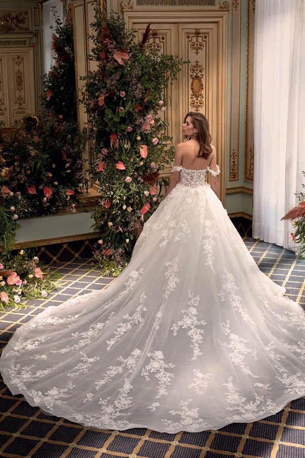 Eine Frau mit langem Haar lächelt in einem opulenten weißen Brautkleid mit Spitze