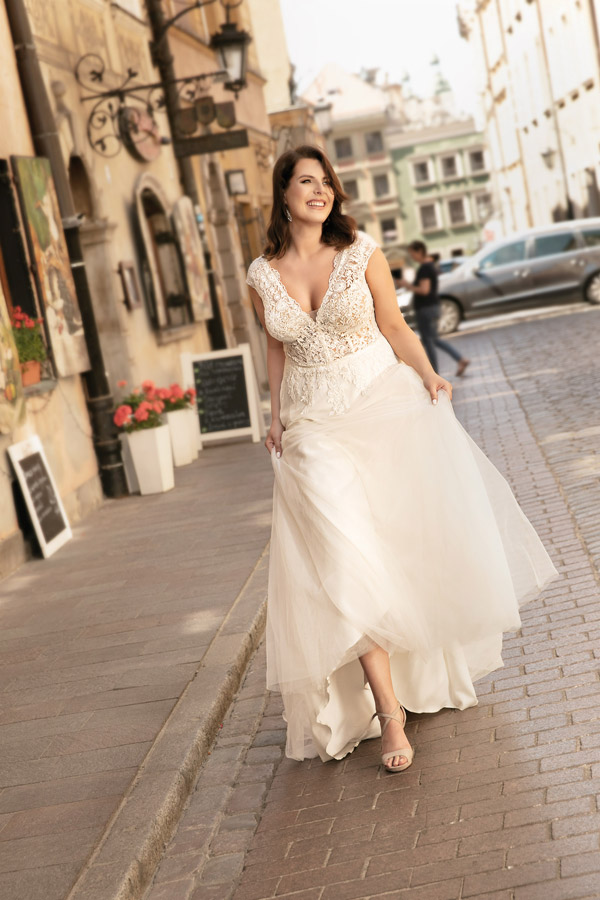 Eine lächelnde Frau trägt ein elegantes weißes Brautkleid auf einer Stadtstraße