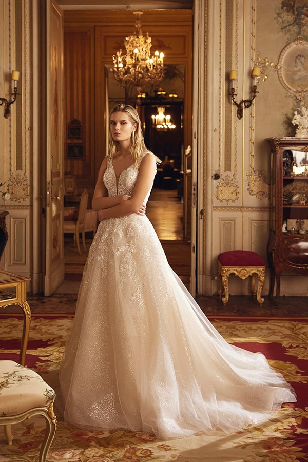 Eine junge Frau mit ernstem Blick trägt ein elfenbeinfarbenes Brautkleid in einem prunkvollen Raum