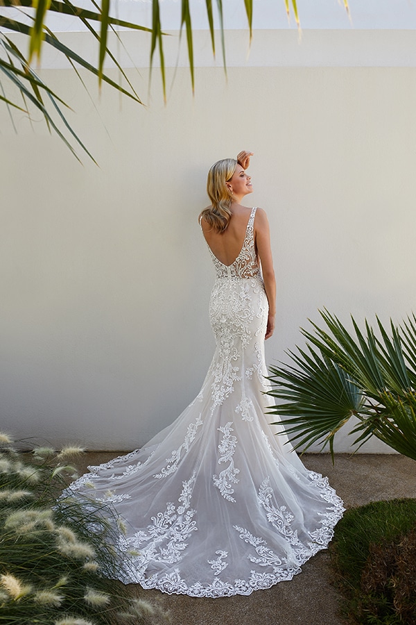 Eine lächelnde Frau im cremefarbenen Spitzenkleid steht vor einer weißen Wand