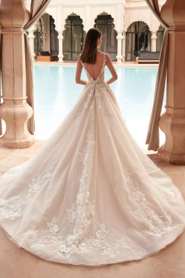 Eine Frau im weißen Spitzenbrautkleid steht träumend vor einem eleganten Pool