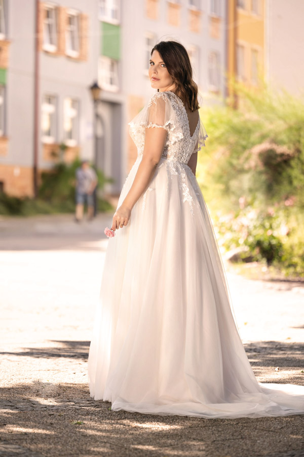 Eine brünette Frau im weißen Brautkleid schaut ernst über die Schulter in die Sonne