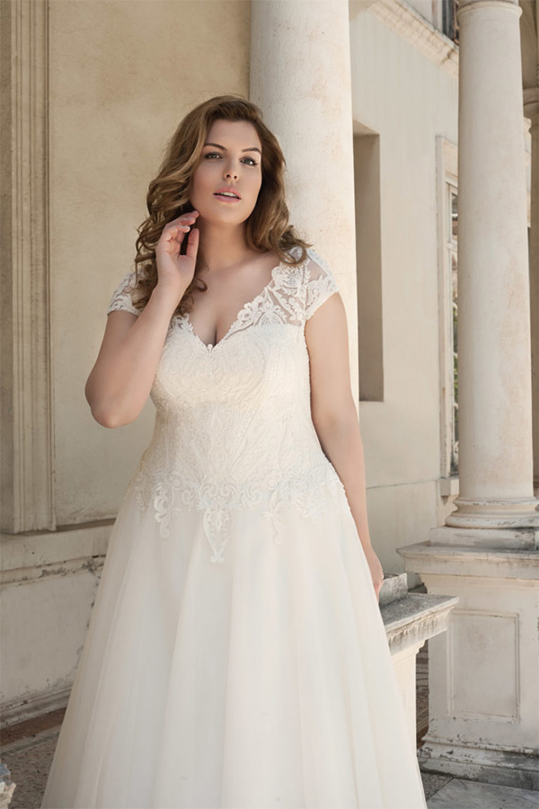 Eine Frau mit langen blonden Haaren trägt ein elegantes weißes Brautkleid und wirkt nachdenklich