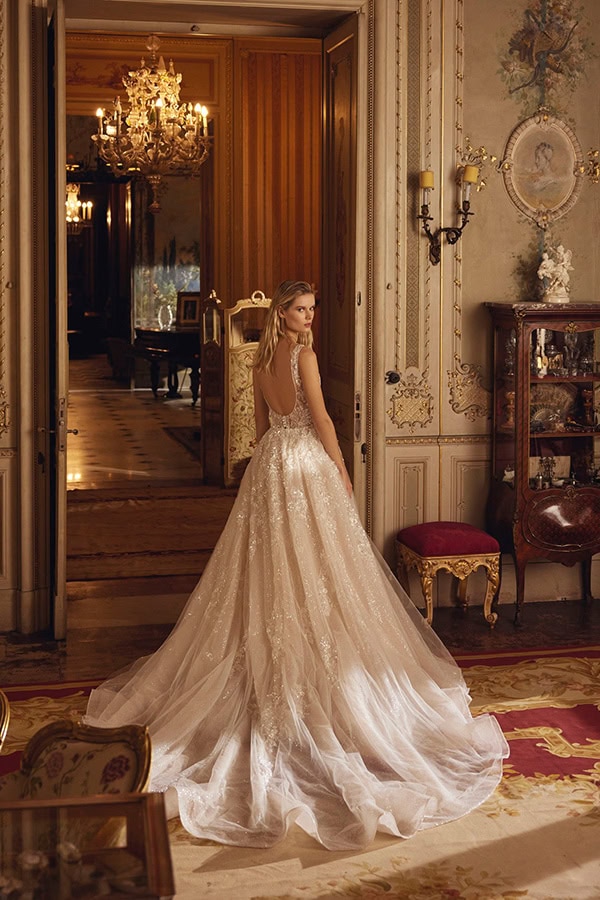 Eine junge Frau im eleganten cremefarbenen Ballkleid steht verträumt in einem prunkvollen Saal