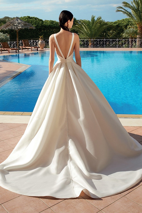Frau mit dunklem Haar in elegantem weißen Kleid steht am Pool mit offenem Rücken