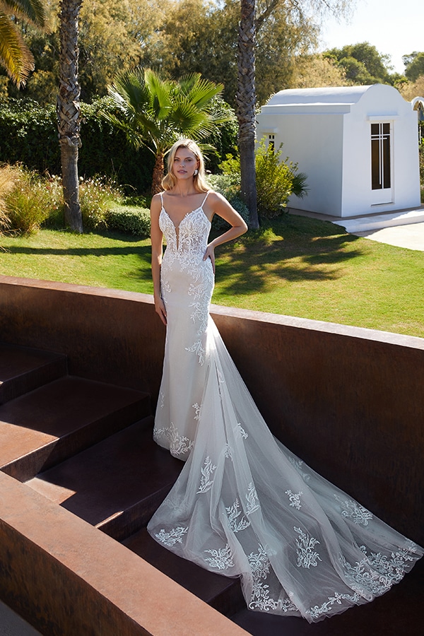 Eine blonde Frau mit ernstem Gesichtsausdruck trägt ein weißes Spitzenbrautkleid im Garten