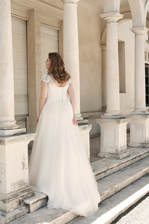 Eine Frau mit langen Haaren trägt ein weißes Brautkleid und steht vor Säulen