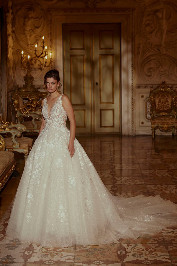 Eine junge Frau im cremefarbenen Brautkleid steht elegant vor prunkvoller Kulisse