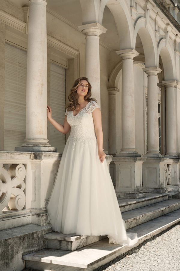 Eine junge Frau im cremeweißen Brautkleid blickt nachdenklich vor Säulen