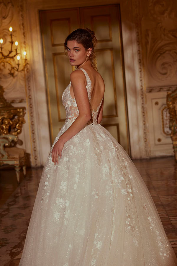 Eine junge Frau mit ernstem Blick trägt ein weißes florales Ballkleid im Prunksaal