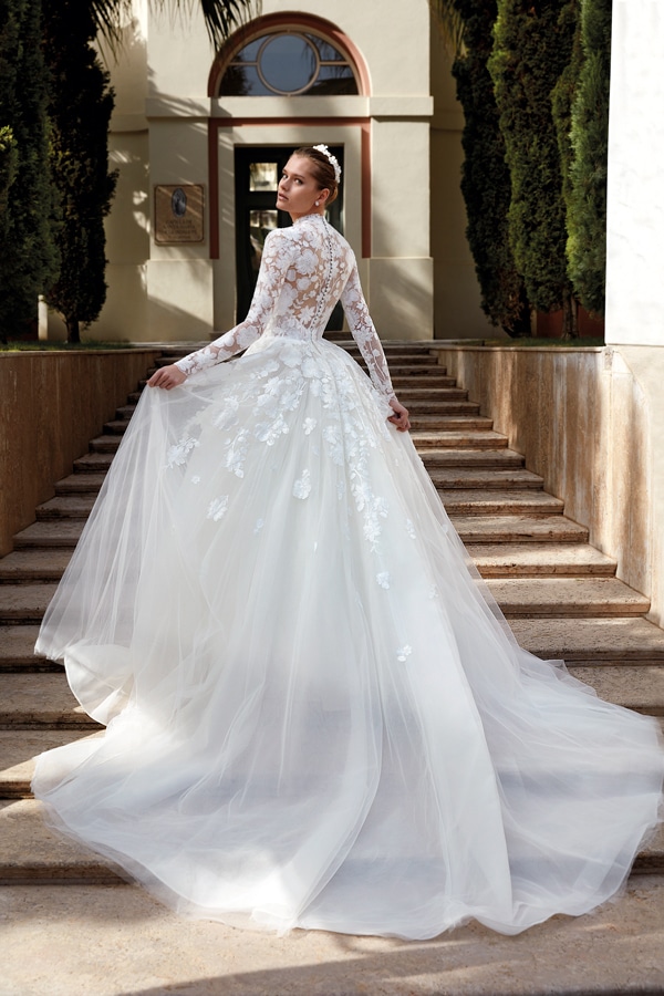 Eine Frau im eleganten Brautkleid mit Spitzenärmeln steht auf einer Steintreppe