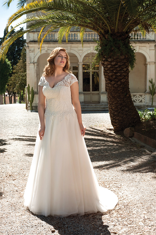 Junge Frau mit welligem blonden Haar trägt ein elegantes weißes Brautkleid im Freien