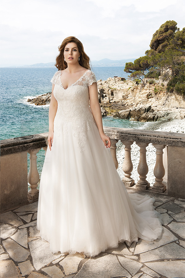 Eine brünette Frau im weißen Brautkleid steht entspannt vor malerischer Meereskulisse