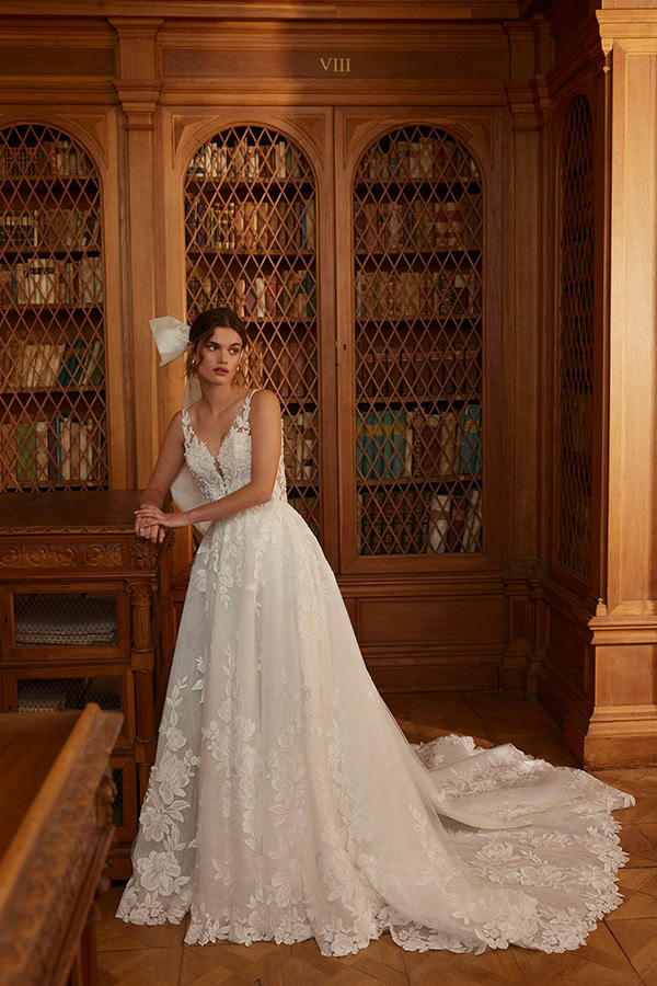 Junge Frau im weißen Spitzenbrautkleid mit Schleier steht nachdenklich in hölzerner Bibliothek