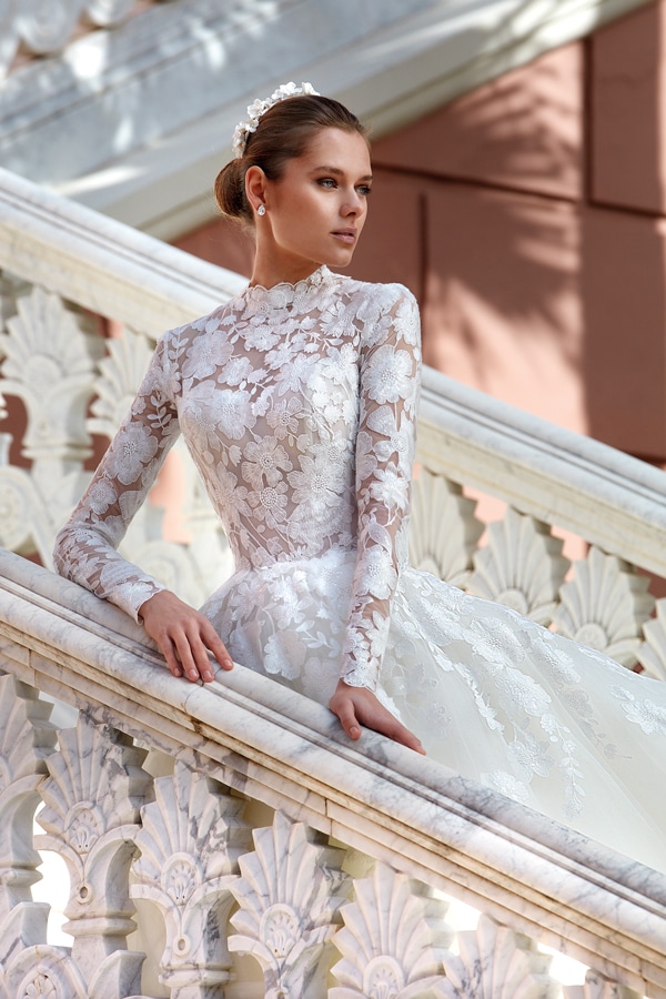 Eine elegante Frau in weißem Spitzenkleid steht ernst auf einer kunstvollen Treppe