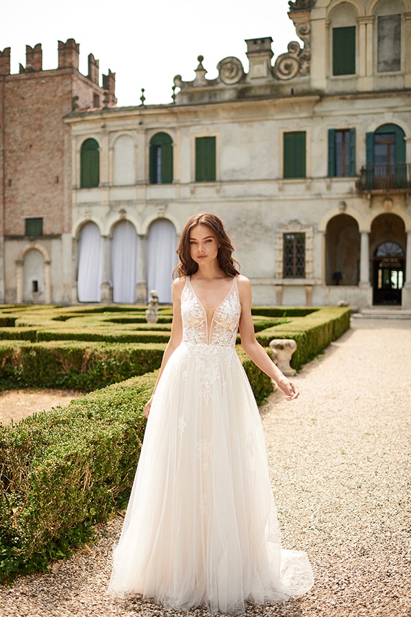 Eine junge Frau mit ernstem Blick trägt ein weißes Brautkleid vor einem Schloss