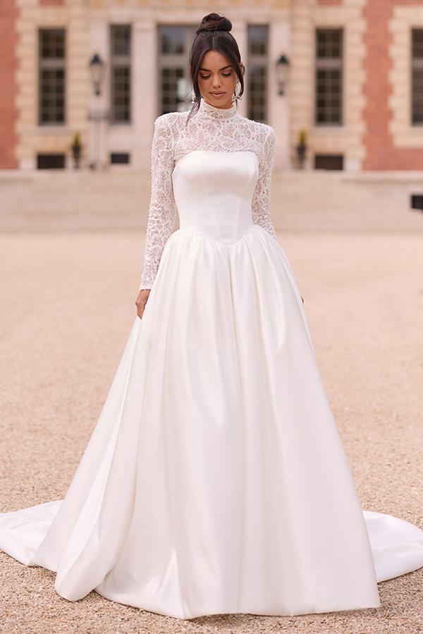 Eine Frau mit ernstem Blick trägt ein langärmeliges weißes Brautkleid aus Satin