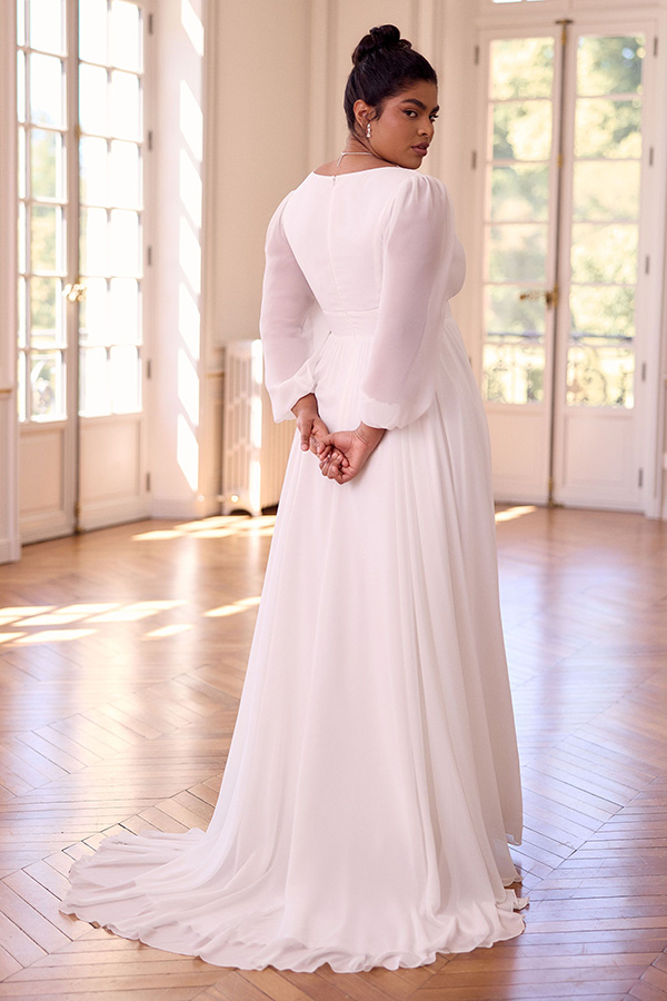 Eine Frau in einem langen weißen Kleid blickt nachdenklich über die Schulter