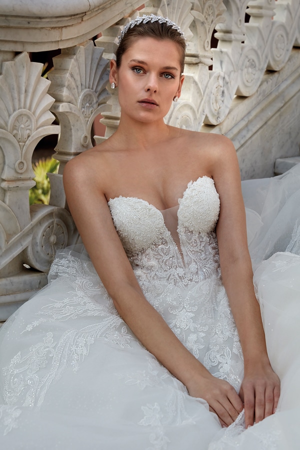 Junge Frau mit ernstem Blick trägt ein weißes Brautkleid und Diadem auf Marmortreppe