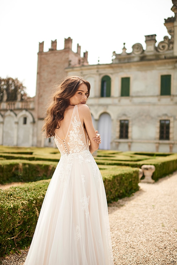Eine junge Frau mit langen braunen Haaren trägt ein elegantes weißes Brautkleid im Garten