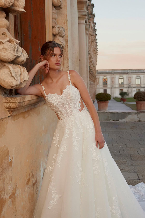 Eine junge Frau mit nachdenklichem Blick trägt ein weißes Spitzenkleid am alten Gebäude