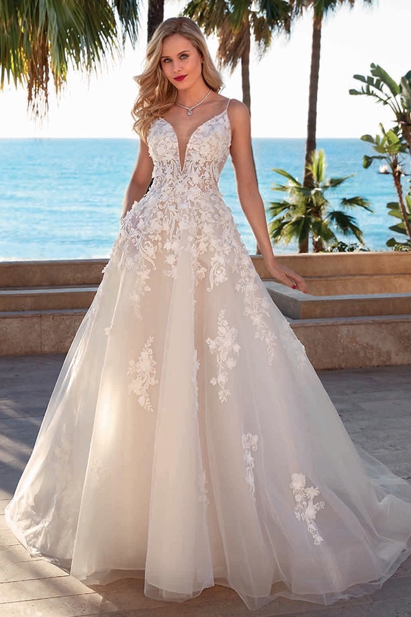 Junge Frau mit langem blonden Haar lächelt in weißem Brautkleid am Strand