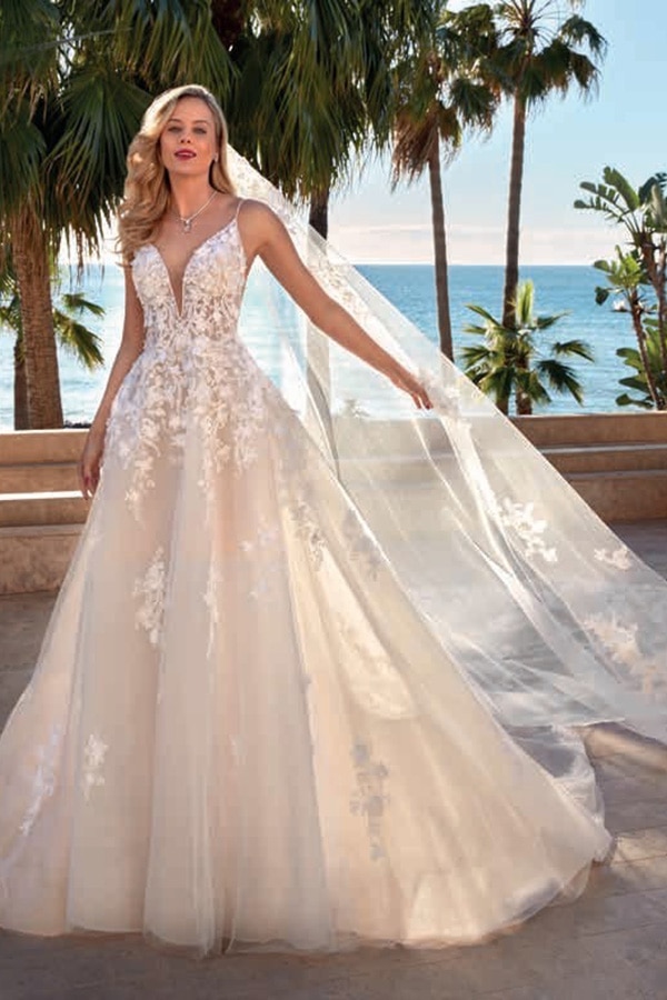 Eine blonde Frau mit hellem Teint trägt ein elegantes weißes Brautkleid und lächelt