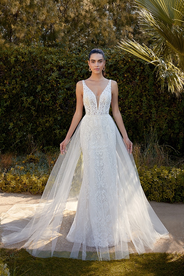 Eine junge Frau mit ernster Miene trägt ein elegantes weißes Brautkleid im Garten