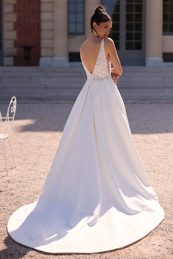 Eine Frau mit elegantem Dutt trägt ein weißes Brautkleid mit Spitzendetails und weitem Rock