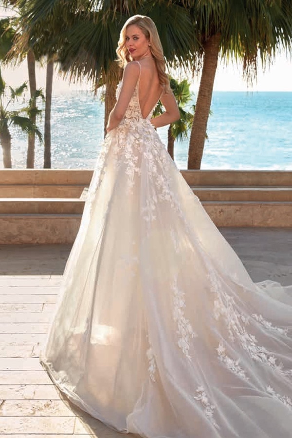 Eine blonde Frau im eleganten Spitzenbrautkleid blickt lächelnd zum Meer