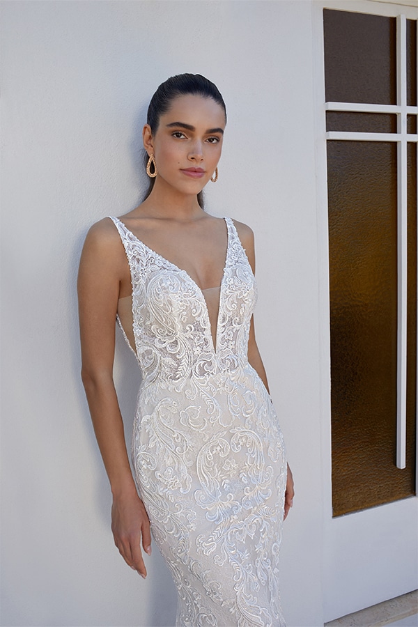 Junge Frau mit ernster Miene in weißem Spitzenkleid vor heller Wand