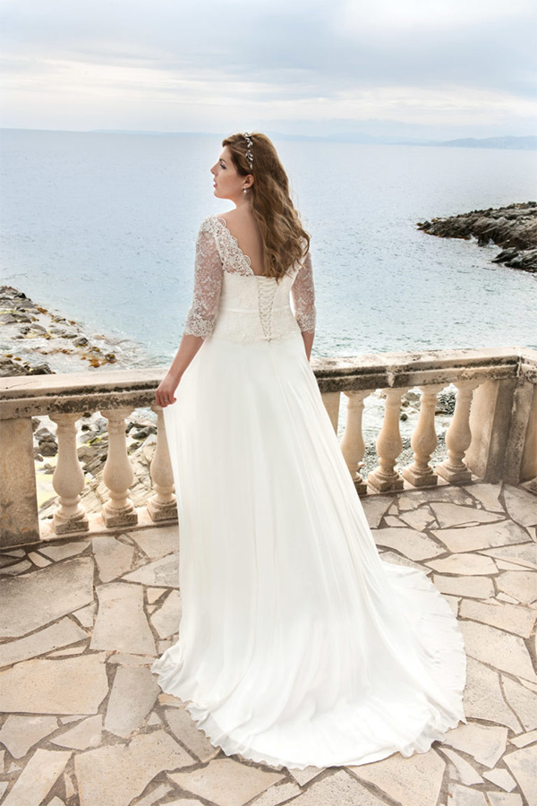 Eine Frau mit langen braunen Haaren trägt ein elegantes weißes Spitzenkleid am Meer