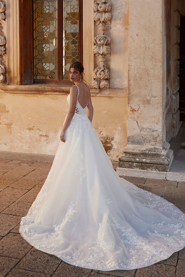 Eine Frau im weißen Brautkleid blickt lächelnd über die Schulter vor altem Gemäuer