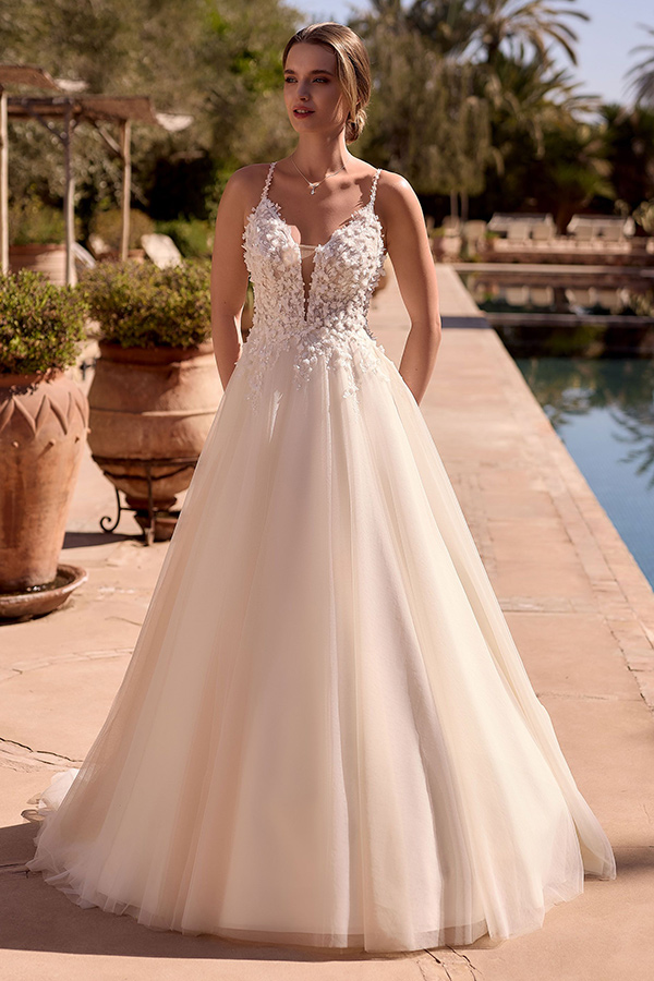 Eine junge Frau mit neutralem Gesichtsausdruck trägt ein cremefarbenes, verziertes Brautkleid