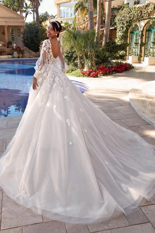 Eine Frau im weißen Spitzenhochzeitskleid lächelt glücklich am Pool in der Sonne