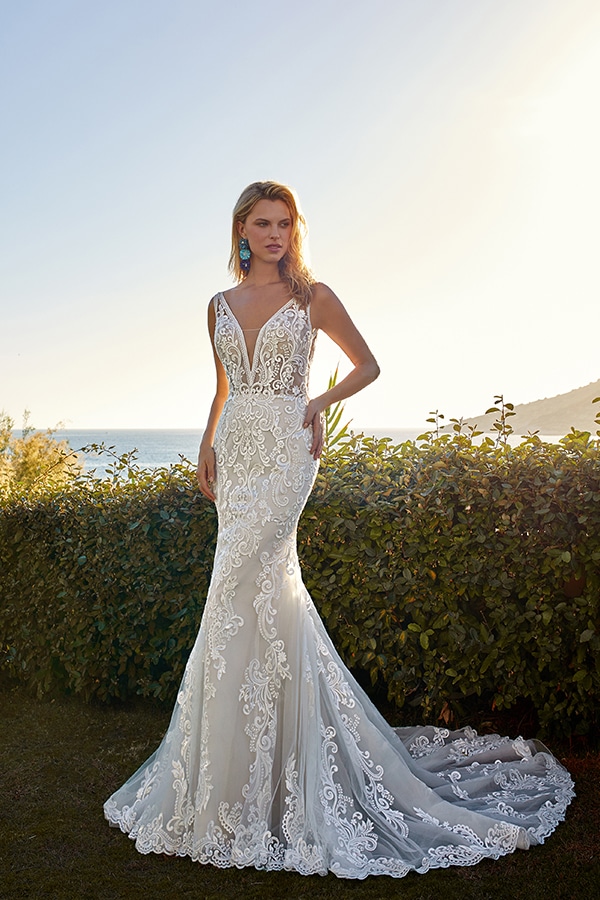 Eine blonde Frau im eleganten weißen Spitzenkleid steht ernst am sonnigen Meer