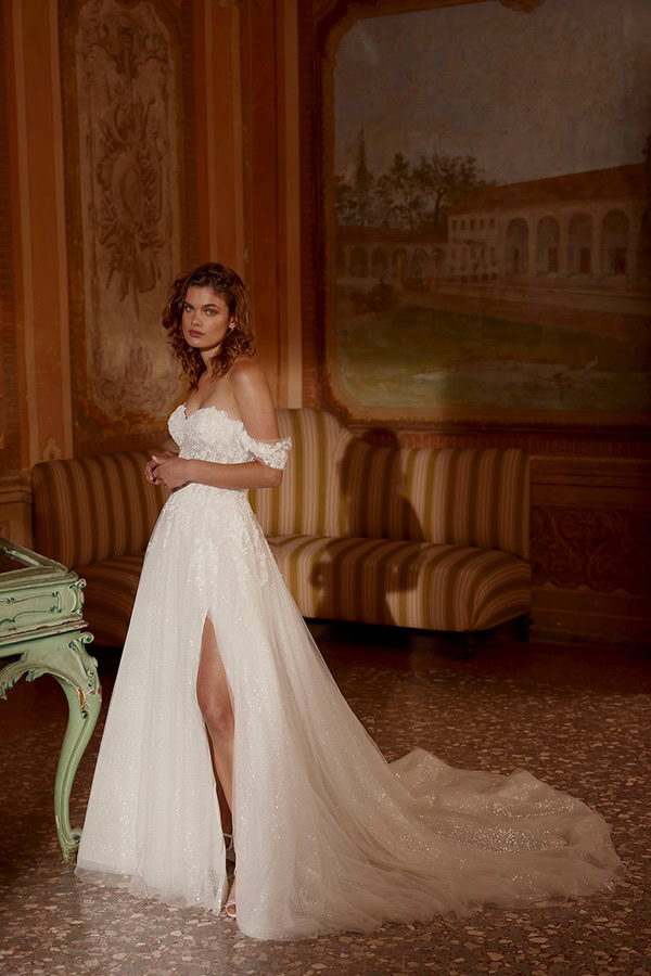 Eine junge Frau mit lockigem braunem Haar steht im hellen Brautkleid im eleganten Raum