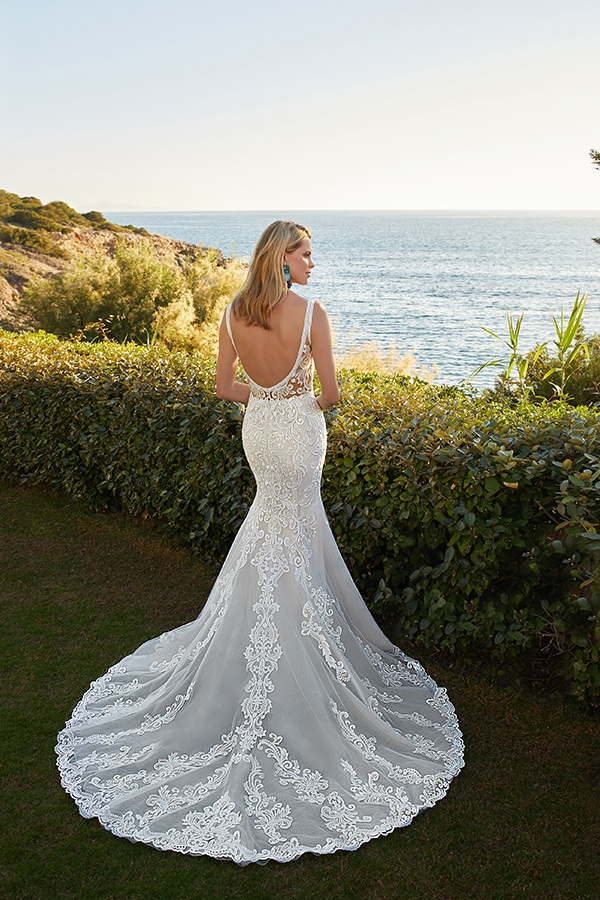 Blonde Frau im eleganten weißen Spitzenkleid steht lächelnd vor dem Meer