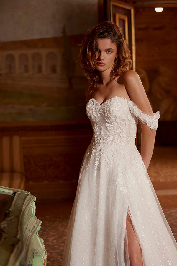 Junge Frau mit nachdenklichem Blick in weißem, schulterfreiem Kleid mit Spitzen und hohem Schlitz